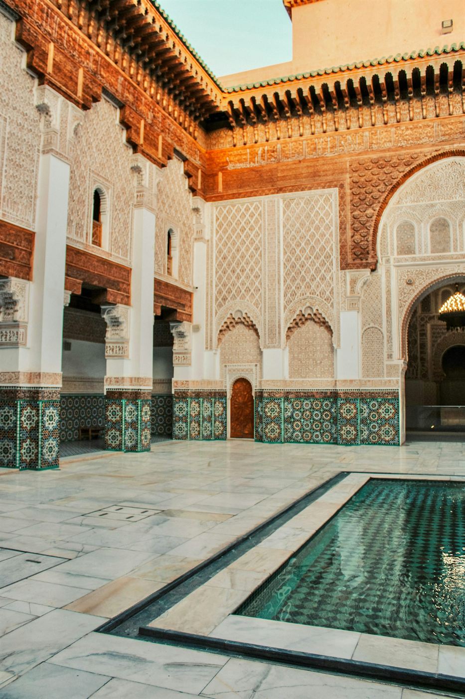 The carved doorway and reflecting pool of a Marrakech madrasa courtyard in warm light