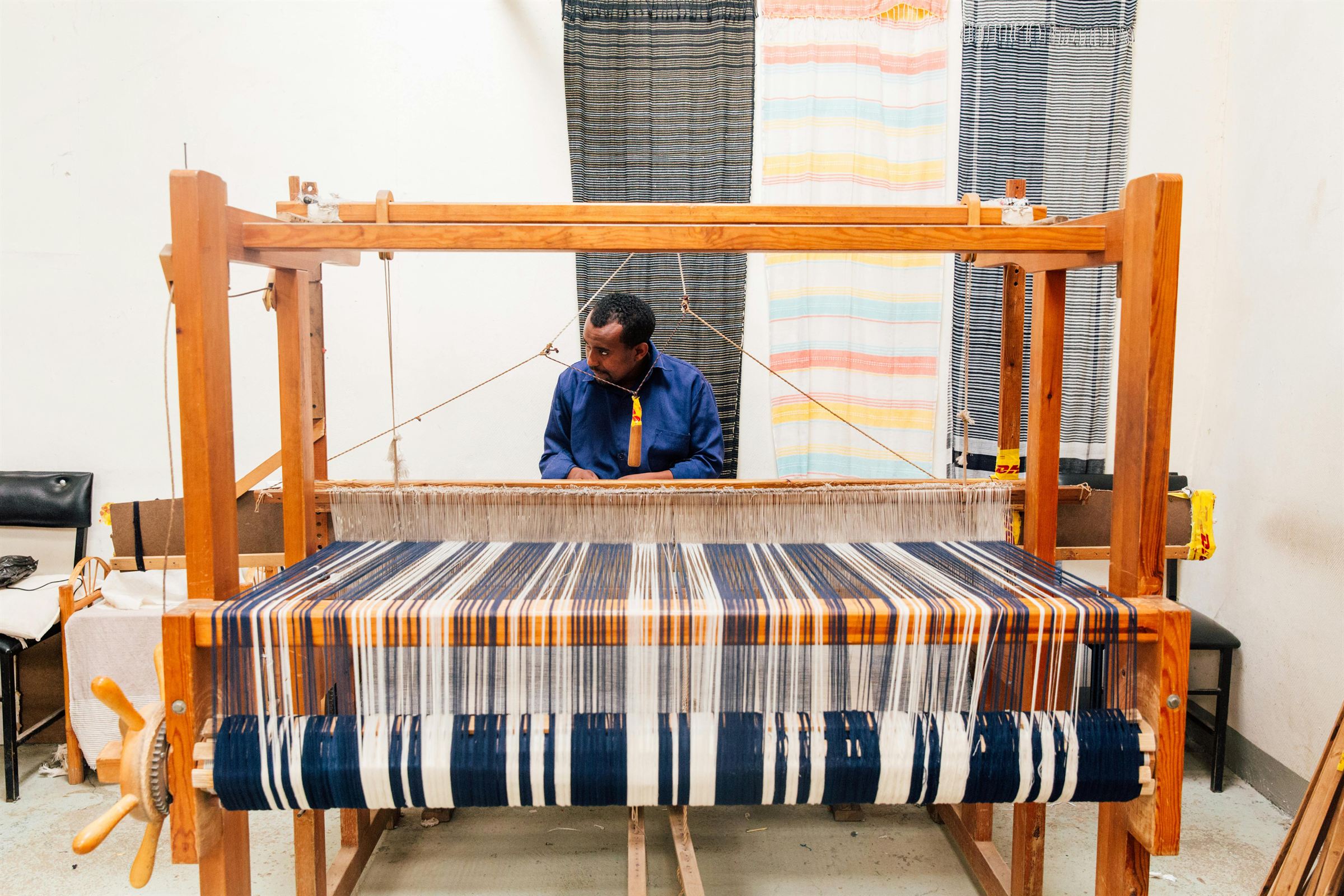 A weaver at a broadloom in Ghana working a length of blue and white striped cloth