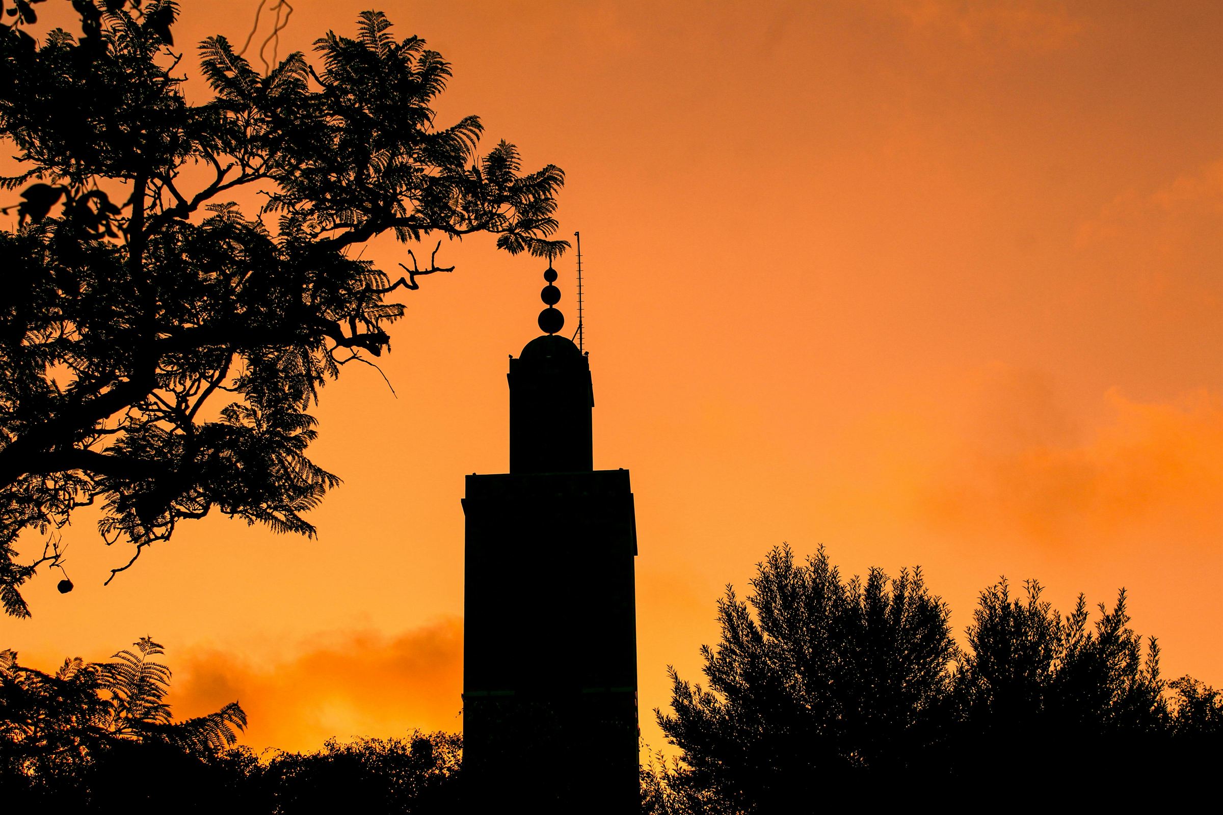 A minaret silhouetted against a deep orange dusk sky in Marrakech